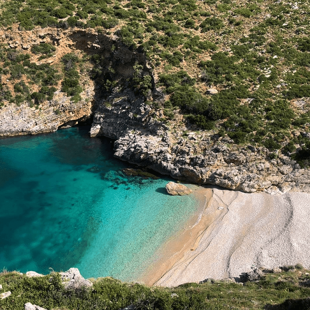 Dafina Bay & National Park Hidden Gems boasts a secluded rocky cove with a small sandy beach, turquoise waters, and lush green vegetation covering the cliffs, creating a picturesque natural setting.