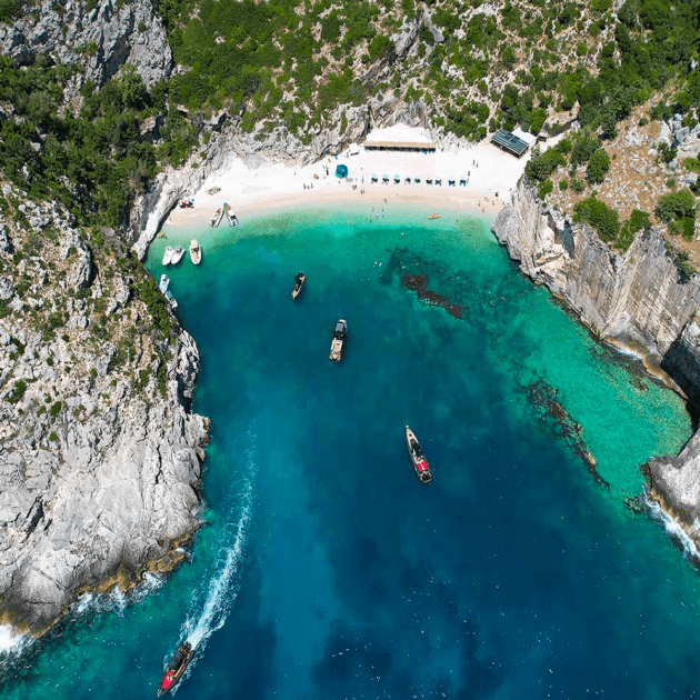 Explore Grama Bay, Blue Cave and Marine Park: a secluded beach encircled by rocky cliffs and lush greenery, with turquoise waters that host small boats. Relax under umbrellas or sunbathe on the sandy shore.
